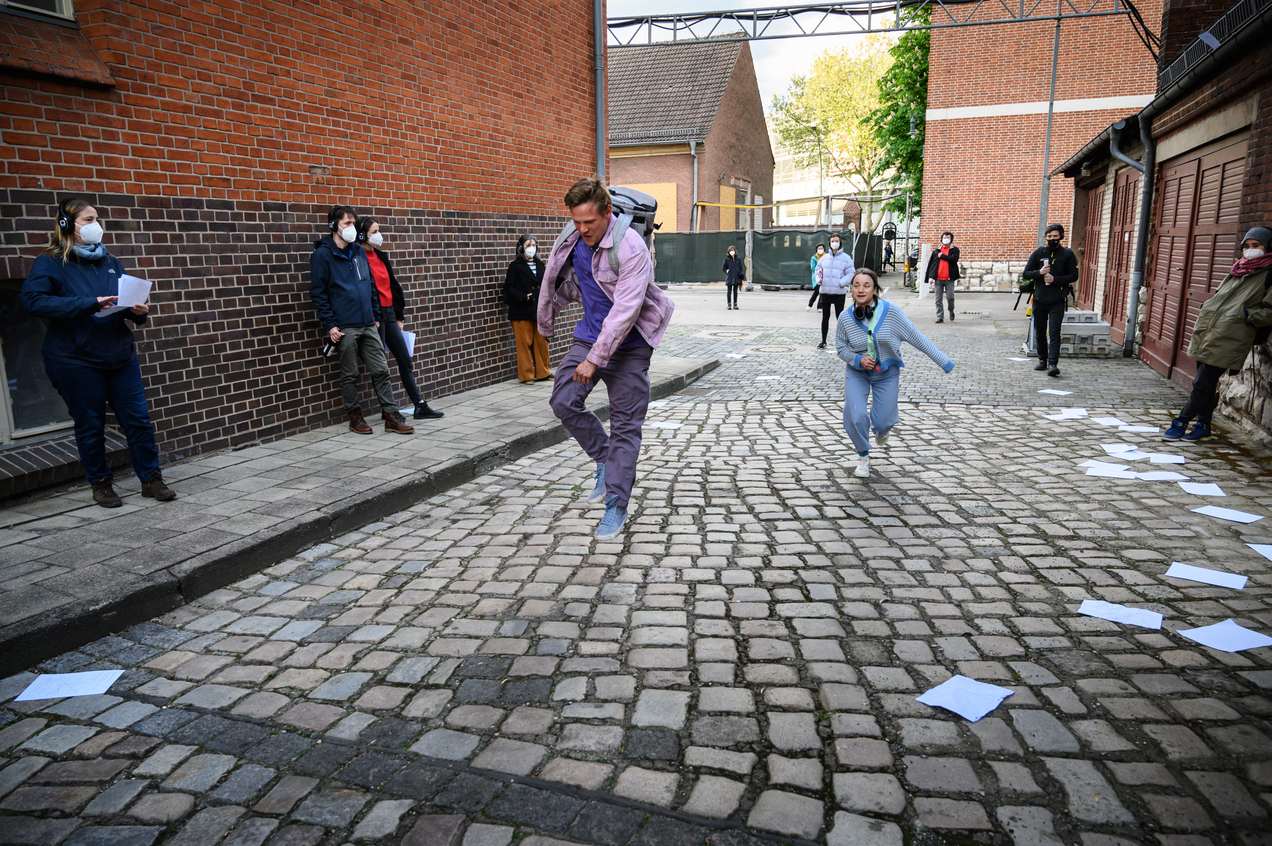 Gruppe von zuschauenden Menschen mit Kopfhörern und zwei schauspielende Personen im Innenhof des Theater Strahl.